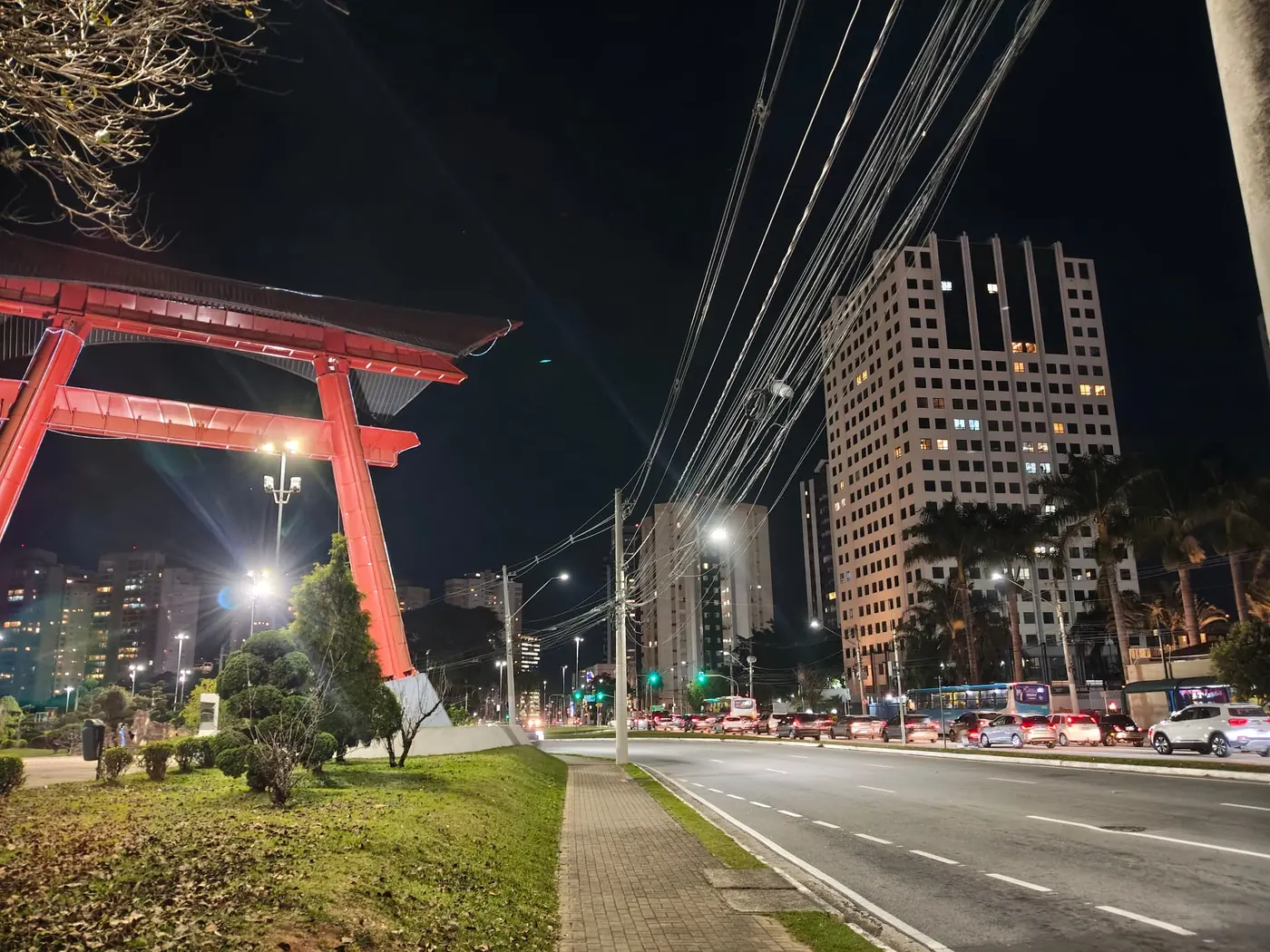 Torii vermelho iluminado à noite na Avenida Cassiano Ricardo, com os prédios do Jardim Aquarius ao fundo